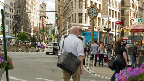 people walking on 5th Ave with famous clock on summer day in Manhattan
