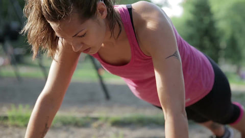 woman in pink tank top doing push-ups in Central Park on warm summer day