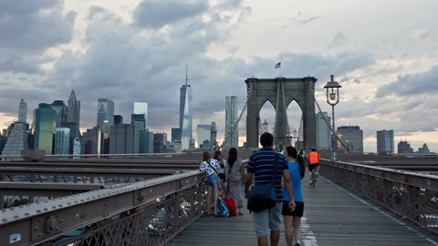 panning across Brooklyn Bridge pedestrian path - people walking in early evening summer day around sunset in NYC