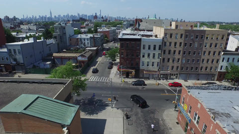 aerial rising up above Brooklyn neighborhood with Manhattan skyline in far distance in NYC