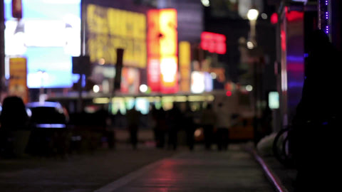 silhouettes of people walking and cars passing in Times Square at night