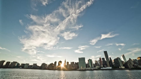 Manhattanhenge - view of Manhattan skyline at sunset from across East River - sun beaming through buildings as it dips