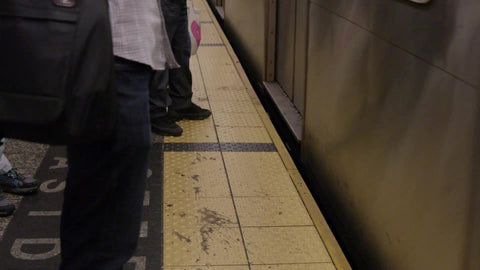 people standing on yellow line on subway platform - man's shoes over line