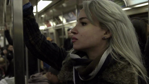 beautiful female passenger riding subway train holding on to metal pole, passengers in background, 1080 HD