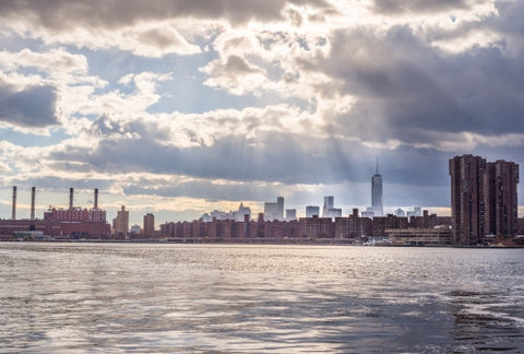 view of Freedom Tower in Manhattan skyline with red brick buildings from across river water - smoke stacks on bright sunny day with blue sky and clouds