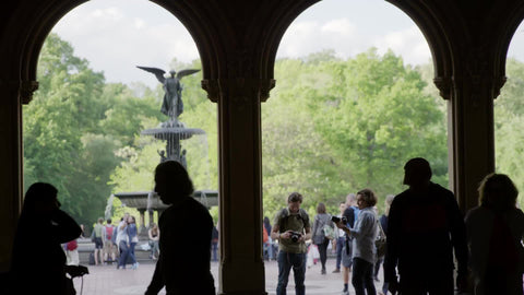 silhouettes under Bethesda Terrace - view of angel statue with wings and water fountain in summer - photographer setting up shot with DSLR camera