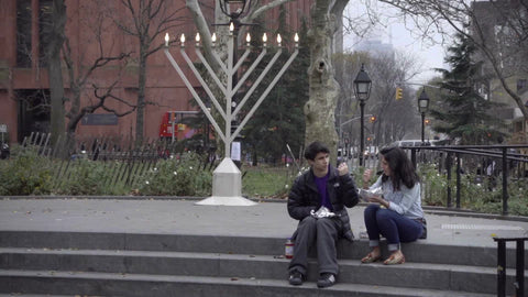 young Jewish couple picnic eating sitting by large Menorah in Washington Square Park on Chanukah in NYC