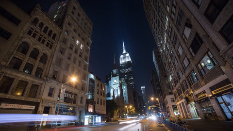 zooming out from Empire State Building lights at night with streaks of cars speeding below - 4K timelapse in Manhattan NYC