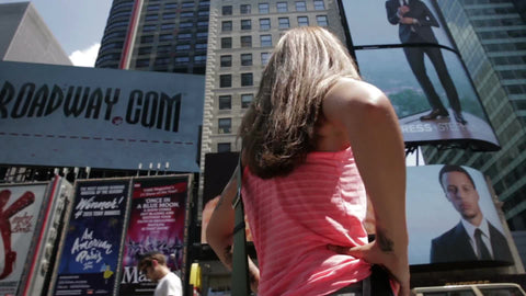 tourist with hands on hips taking in the Big Apple, traveler woman with sunglasses looking up at Times Square ads and signs in Manhattan