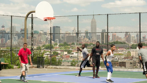kid shooting and scoring jump shot playing basketball on court overlooking Manhattan skyline in NYC with Empire State Building on summer day