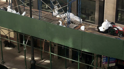 scaffolding on side of building with construction workers in yellow hardhats climbing and working in NYC