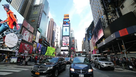 cars driving in Times Square traffic on bright sunny day with blue sky and clouds