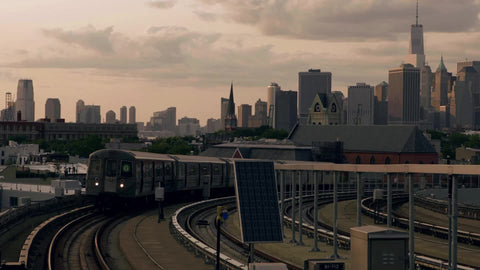 G train arriving at Smith-Ninth Street elevated subway station in Brooklyn with Manhattan skyline in background at sunset in NYC