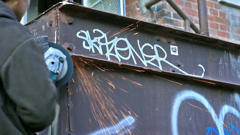 man smoothing edge of metal dumpster with graffiti - sparks from industrial tool - equipment