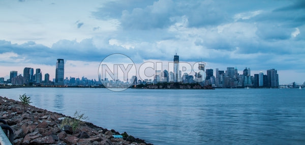 Downtown Manhattan skyline with skyscrapers and East River water view from Brooklyn with rocks in foreground in early evening