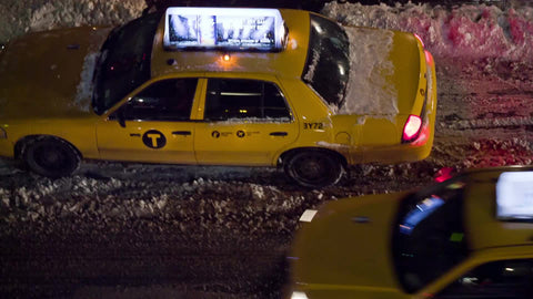 taxi cab driving off in snow storm on slush in street - winter night overhead view in NYC