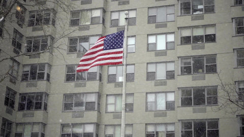 American flag waving in front of city building snowing in winter NYC