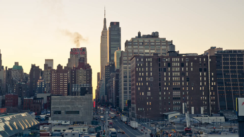 slow zoom out from Empire State Building and construction site with crane at sunset in Midtown Manhattan - 4K timelapse with cars driving in NYC