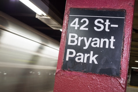 subway column sign for 42nd st and Bryant Park on platform with motion blur train leaving station