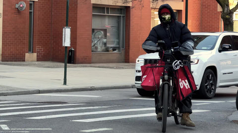 Grub Hub delivery person on bicycle with mask and red bag of food delivering in New York City NYC