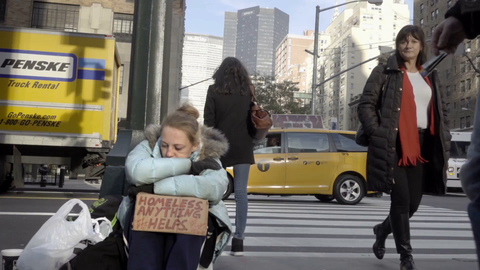 man giving homeless woman with sign a dollar and metro card on Park Ave with MetLife Building in background, Manhattan New York City