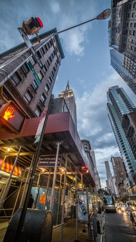 5th Ave with upward angle of towering Empire State Building in early evening with night lights on - lit up