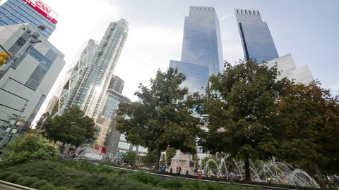 driving around Columbus Circle center fountain in summer with skyscrapers towering over trees