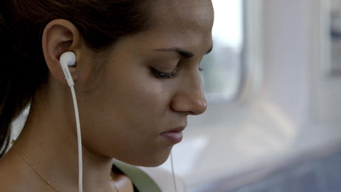 tight shot on woman's face with earbuds listening to music while riding subway train, fingers tapping on smartphone screen