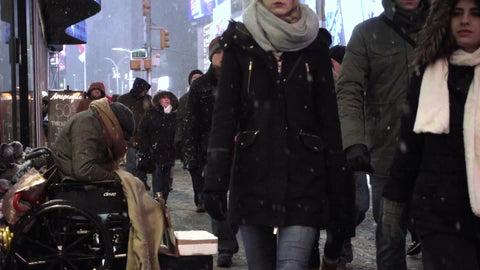 sad homeless man disabled in wheelchair on cold night - snowing in Times Square with tourists walking by ignoring tragedy