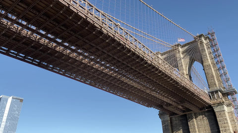 panning across underneath Brooklyn Bridge upward low angle American flag in sky New York City NYC