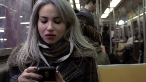 woman on smartphone texting with smirk as subway train is leaving station platform NYC
