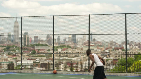 reverse slam dunk on summer day with Empire State Building view through New Jersey fence - man dunking on basketball court