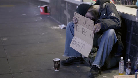 homeless man sleeping with sign in hand on street at night