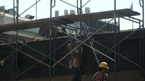 construction workers working together on scaffolding carrying ladder up side of building in NYC
