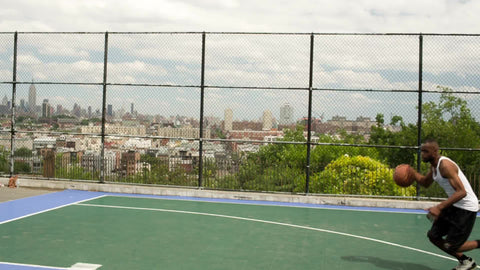 young man slam dunking with two hands - two-handed dunk in summer basketball court with Empire State Building in background