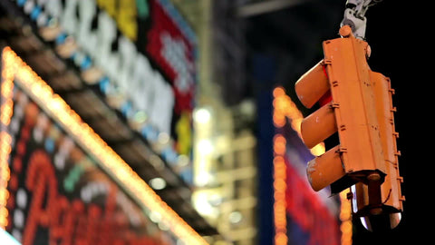 close-up of traffic light hanging on intersection with bright billboards and ads lit up in background at night in Times Square