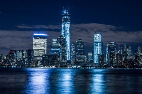 Downtown Manhattan skyline with Freedom Tower and skyscrapers at night reflections off East River water
