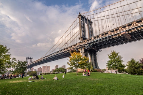 Manhattan Bridge and people lying on green grass of Brooklyn Bridge Park on summer day in NYC