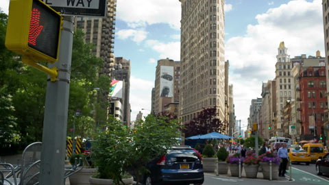 Flatiron Building on 5th Ave and Broadway with cars and taxicab driving in summer