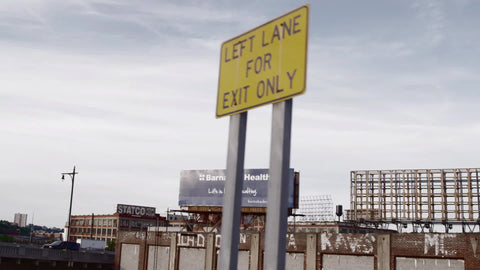 left lane for exit only sign in Brooklyn with gritty buildings with vandalism from driving car view