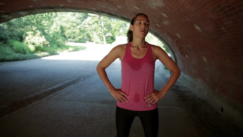 female runner catching breath in Central Park underpass while kid on scooter and father ride by