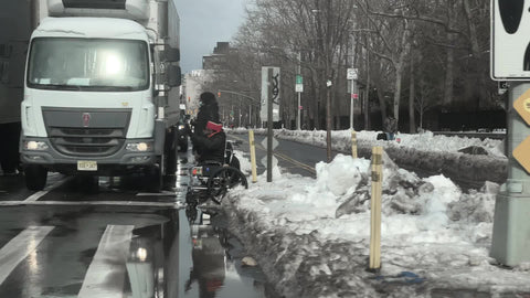 driving past trucks and homeless person sitting on sidewalk with snow in cold New York City winter NYC