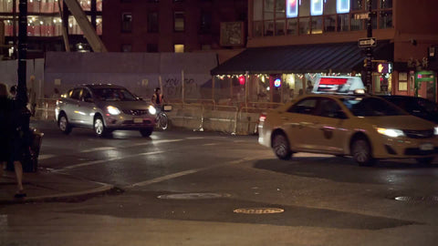 nightlife on street corner - girls walking by and cars and cabs driving in traffic on summer night in Manhattan NYC