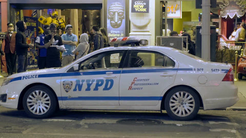 NYPD police car parked outside store in summer with people hanging out