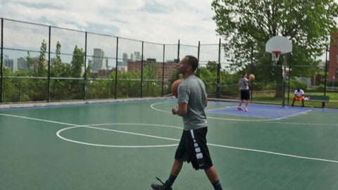 pickup game on summer day with view of Manhattan skyline in NYC through basketball court fence