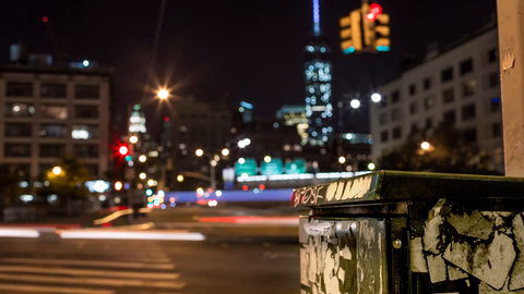 green phone box and busy intersection in Downtown Manhattan with Freedom Tower out of focus in background - 4K timelapse at night in NYC