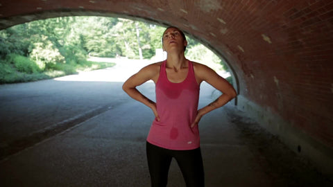 runner with hands on hips catching breath and sweating under bridge in Central Park after exercise