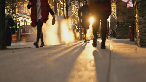 people walking over steam grating with bright sun in New York City