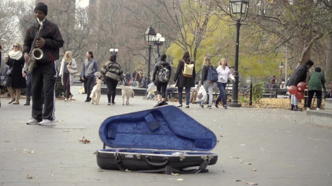 musician playing saxophone in Washington Square Park with open sax case for donations