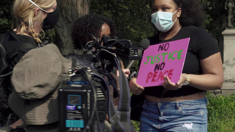 Black woman being interviewed with no justice no peace sign at BLM rally in New York City